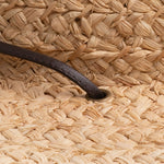 Close-up of a natural colored straw hat with a brown leather drawstring going into a golden colored eyelet