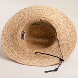 Underside of a natural colored straw hat with a wide brim and loose brown leather drawstrings on a light beige background