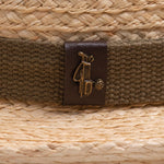 Close-up of a natural colored straw hat with a brown band and logo, featuring a golden colored golf club bag and golf ball ball pin on top of it