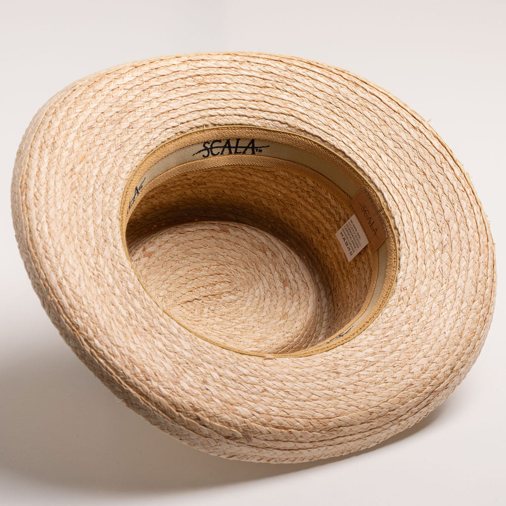 Underside of a natural colored straw hat with a golden colored sweatband on a light beige background