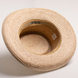 Underside of a natural colored straw hat with a golden colored sweatband on a light beige background