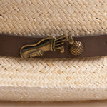Close-up of a natural colored straw hat with a decorative band featuring a golden colored golf club and ball pin