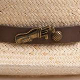 Close-up of a natural colored straw hat with a decorative band featuring a golden colored golf club and ball pin