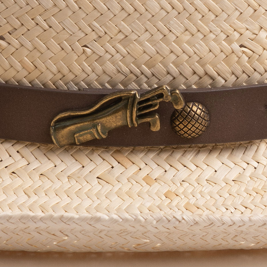 Close-up of a natural colored straw hat with a decorative band featuring a golden colored golf club and ball pin