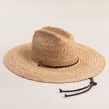 Natural colored straw hat with a wide brim and brown loose drawstrings on a light beige background