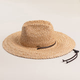 Natural colored straw hat with a wide brim and brown loose drawstrings on a light beige background