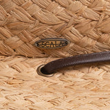 Close-up of a natural colored straw hat with a Scala logo pin and a brown leather strap going into a golden colored eyelet