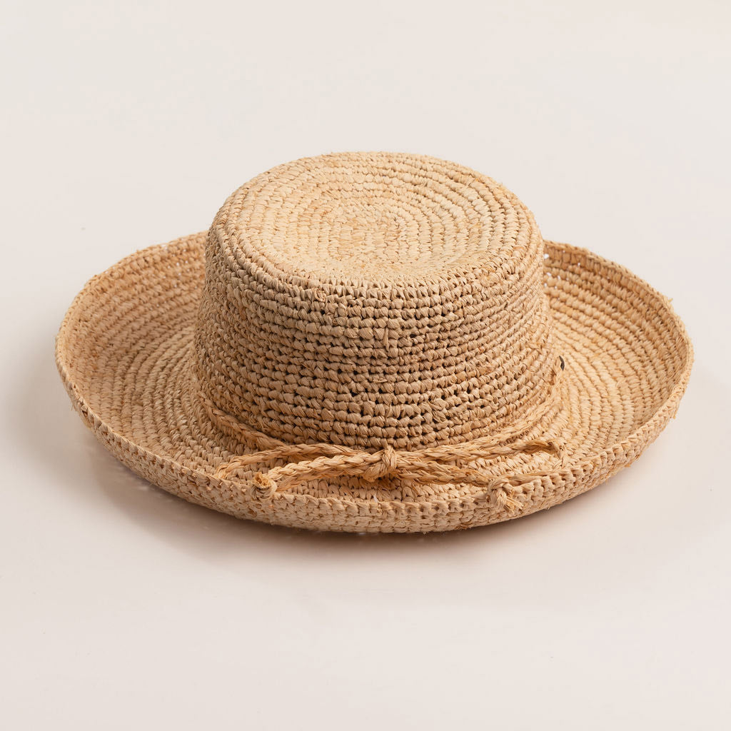 Natural colored straw hat with the straw ribbon band facing front on a light beige background