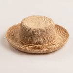 Natural colored straw hat with the straw ribbon band facing front on a light beige background