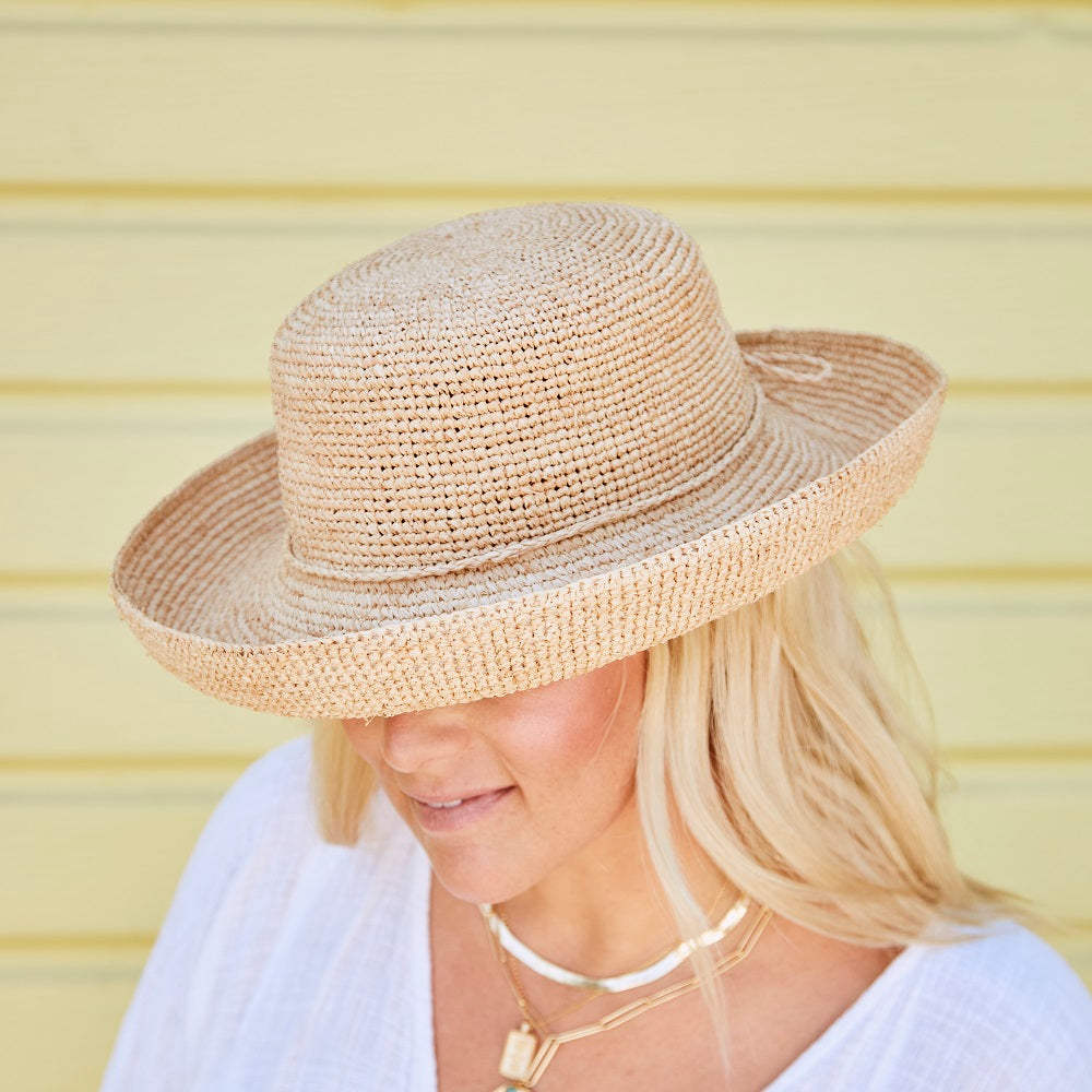 Woman wearing a natural colored straw hat facing downwards against a yellow striped background