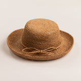 Tea colored straw hat with the straw ribbon band facing front on a light beige background