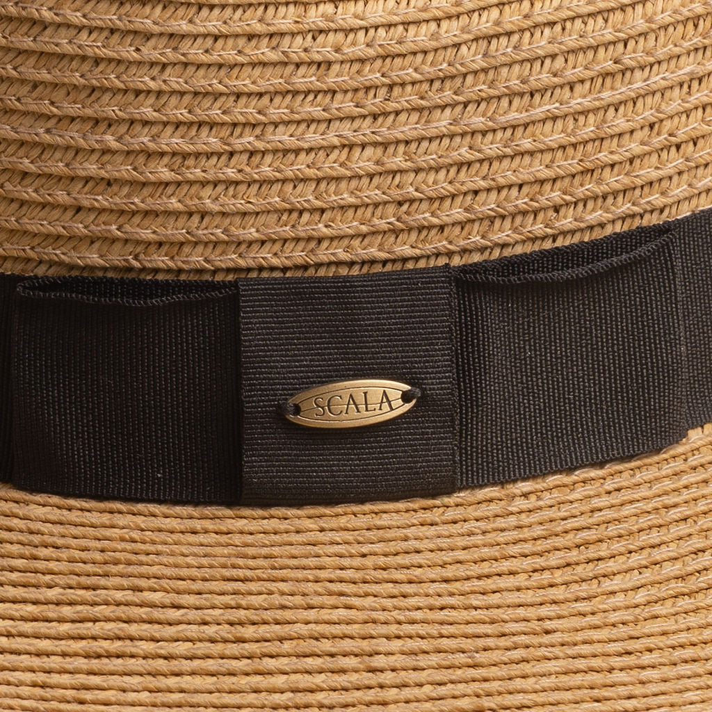 Close-up of a toast colored straw hat with a black band and Scala logo pin