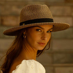 Woman wearing a toast colored straw hat with a blurred background