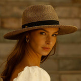 Woman wearing a toast colored straw hat with a blurred background