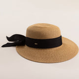 Tea colored straw hat with a thick black ribbon on a light beige background