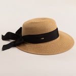 Tea colored straw hat with a thick black ribbon on a light beige background