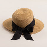 Tea colored straw hat with a thick black ribbon on a light beige background