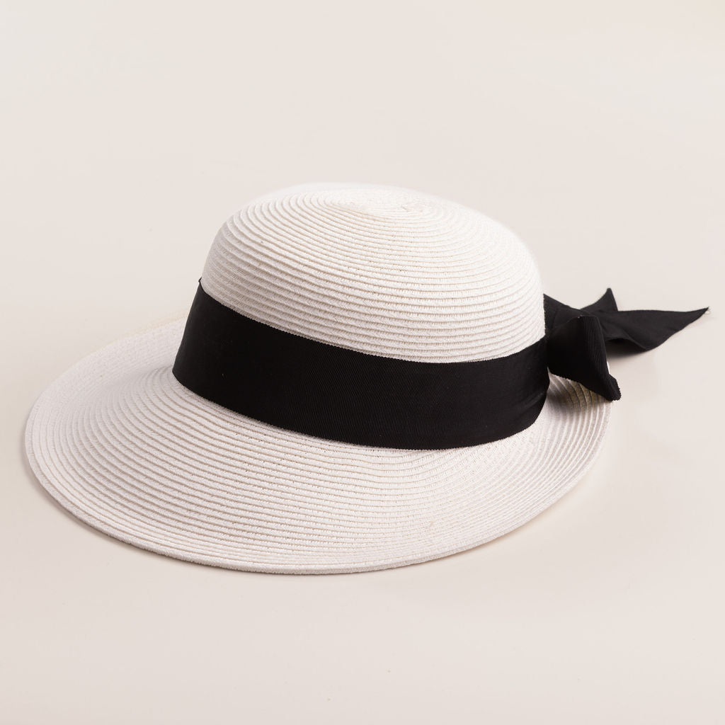 White straw hat with a thick black ribbon on a light beige background