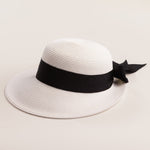 White straw hat with a thick black ribbon on a light beige background