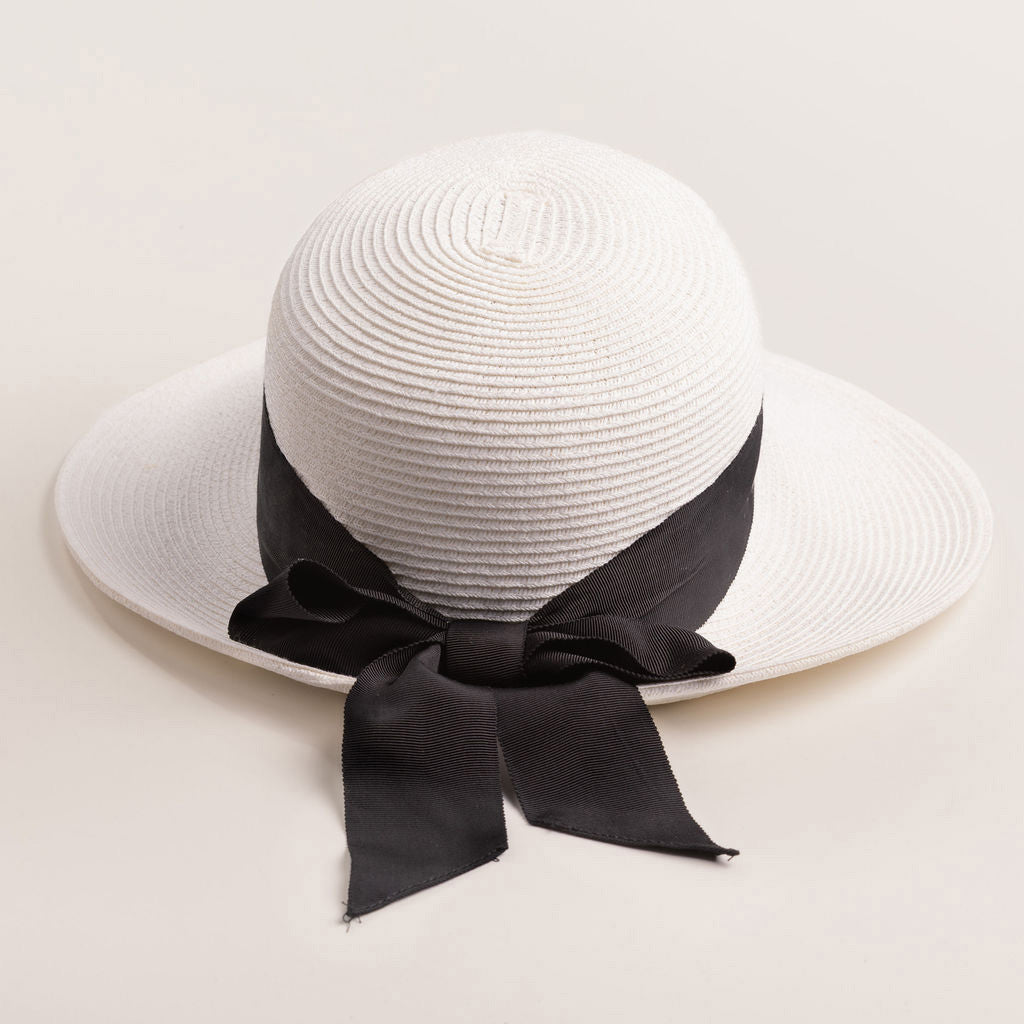 White straw hat with a thick black ribbon on a light beige background