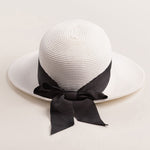 White straw hat with a thick black ribbon on a light beige background