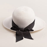 White straw hat with a thick black ribbon on a light beige background