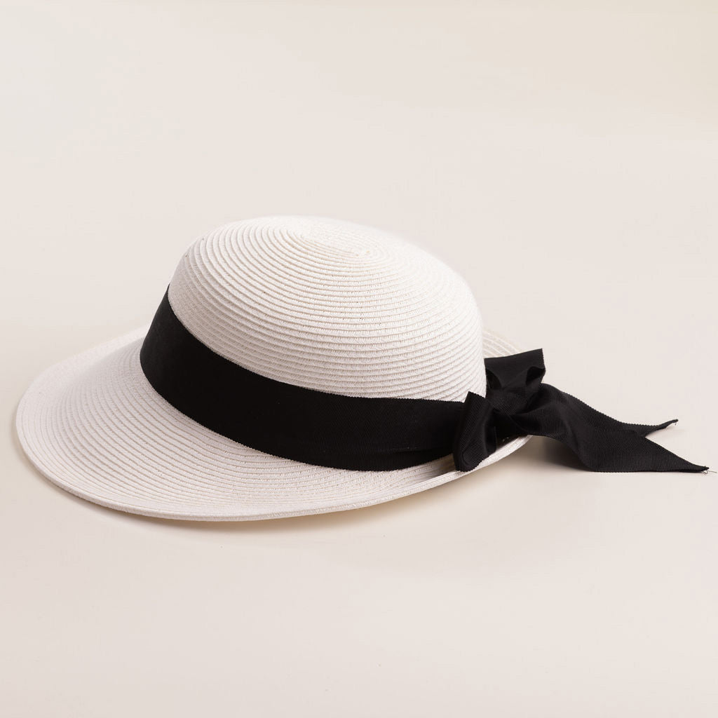 White straw hat with a thick black ribbon on a light beige background