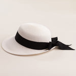White straw hat with a thick black ribbon on a light beige background