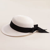 White straw hat with a thick black ribbon on a light beige background