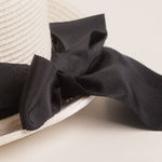 Close-up of a black ribbon bow on a white straw hat