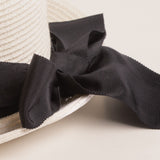 Close-up of a black ribbon bow on a white straw hat