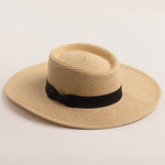Natural colored straw hat with a black band on a light beige background