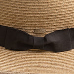 Close-up of a natural colored straw hat with black ribbon and Scala pin logo