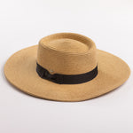 A natural straw sun hat with a black ribbon band and bow, photographed on a clean light gray background