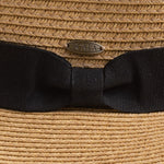 Close-up of a woven straw hat with a wide black ribbon bow and a small oval Scala brand pin at the center