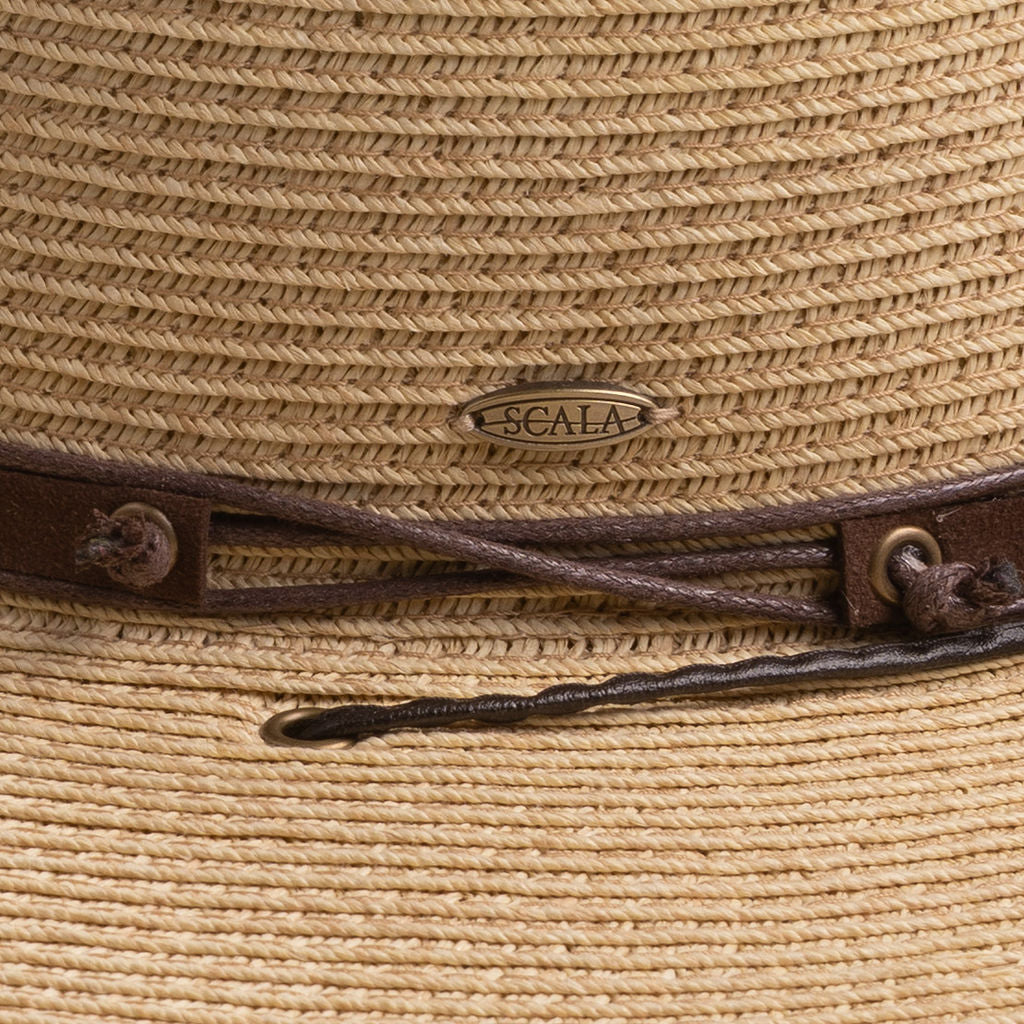 Close-up of a natural colored straw hat with the Scala logo pin and brown drawstring going into a golden colored eyelet
