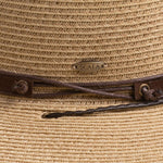 Close-up of a natural colored straw hat with the Scala logo pin and brown drawstring going into a golden colored eyelet