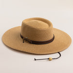 Toast colored straw hat with a brown band on a light beige background