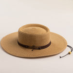 Toast colored straw hat with a brown band on a light beige background