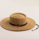 Toast colored straw hat with a brown band on a light beige background