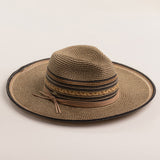 Multi-colored straw hat in shades of brown and black with a wide brim on a light beige background