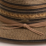 Close-up of a multi-colored straw hat in shades of brown and black with a ribbon tie on and Scala logo pin