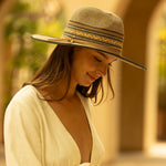 Woman wearing a multi-colored straw hat in shades of brown and black facing downward with a blurred background