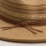 Close-up of a natural colored straw hat in shades of brown with a brown ribbon and Scala logo pin