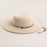 Ivory colored straw hat with a black band on a light beige background