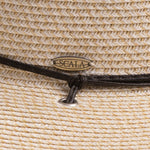 Close-up of an ivory colored straw hat with the Scala logo pin and black band going into a silver eyelet