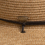 Close-up of a natural colored straw hat with a Scala logo pin, featuring a brown braided drawstring going into a gold eyelet