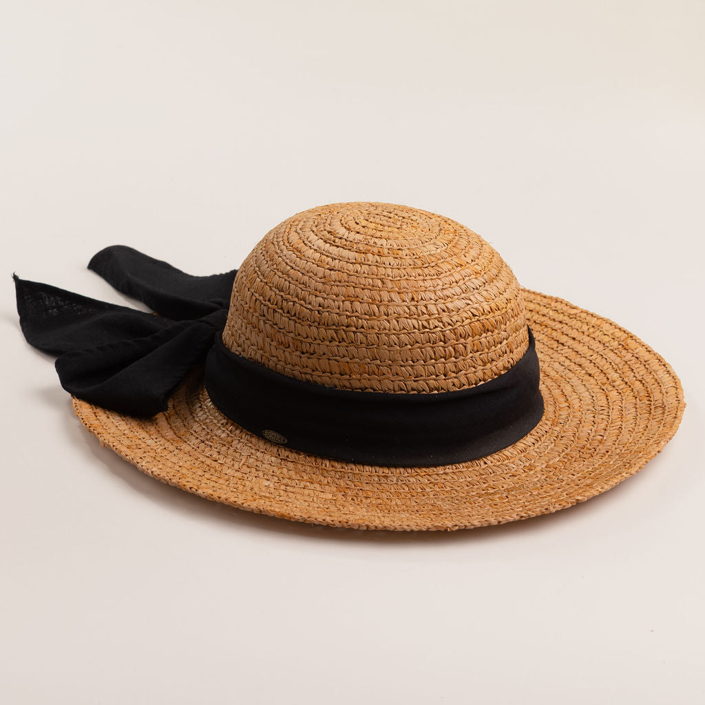 Tea colored colored straw hat with a thick black ribbon on a light beige background