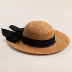 Tea colored colored straw hat with a thick black ribbon on a light beige background