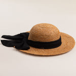 Tea colored colored straw hat with a thick black ribbon on a light beige background